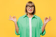 Elderly blonde woman 50s years old wear green shirt glasses casual clothes hold spread hands in yoga om aum gesture relax meditate try calm down isolated on plain yellow background. Lifestyle concept.