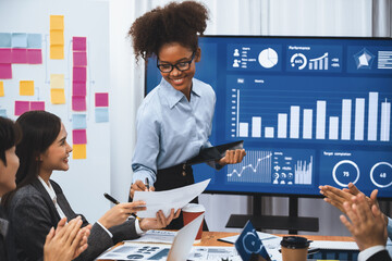 Wall Mural - Young african businesswoman presenting data analysis dashboard on TV screen in modern meeting. Business presentation with group of business people in conference room. Concord