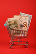 World paper currencies in shopping cart over red