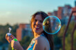 © Jelena - Young attractive brunette with necklace making bubbles on the roof with a city view. Back to the childhood