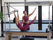 Asian woman doing pilates with trainer on cadillac reformer. 