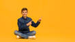 Smiling teen boy sitting on floor and pointing aside at copy space