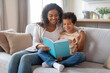 © Prostock-studio - Family leisure activity. Young black mother and little son reading book together