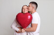 © sementsova321 - Loving couple celebrating anniversary man and woman with heart shaped balloon isolated over grey background husband kissing smiling wife cheek enjoying romantic moments