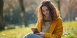 © T-elle - Smiling young woman in a yellow hoodie enjoying her phone in a sunny daisy field