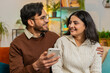 © Andrii Iemelianenko - Multiracial young couple sitting on sofa and swipe smartphone at home. Happy Hispanic man and woman discussing together spend time, relaxing and enjoying communicate on mobile phone in room apartment