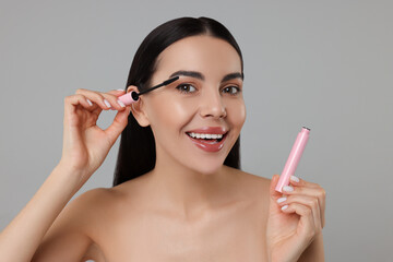 Canvas Print - Beautiful young woman applying mascara on grey background