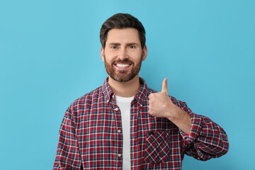 Poster - Portrait of smiling man with healthy clean teeth showing thumb up on light blue background