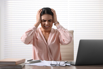 Canvas Print - Young woman suffering from headache at wooden table in office