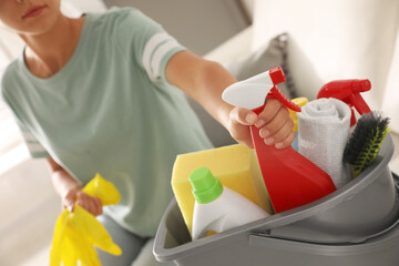 Canvas Print - Woman taking bottle of detergent from bucket with cleaning supplies indoors, closeup