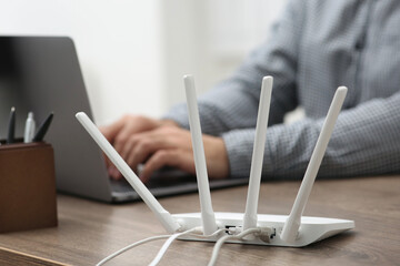 Man with laptop working at wooden table indoors, focus of Wi-Fi router
