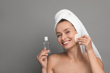 Wall Mural - Smiling woman removing makeup with cotton pad and holding bottle on grey background. Space for text