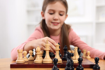 Poster - Cute girl playing chess at table indoors, selective focus