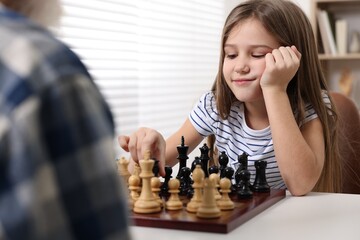 Girl playing chess with her grandfather at table in room