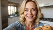 Happy middle-aged blonde woman smiling while holding freshly baked muffins in a bright kitchen.