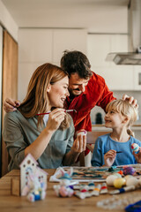 Smiles all around as parents guide their child in the art of Easter egg decoration in the dining room