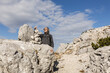 © Guzel - Gray-haired long-haired man building a tower of stones against the background of a picturesque sky and a rocky mountain