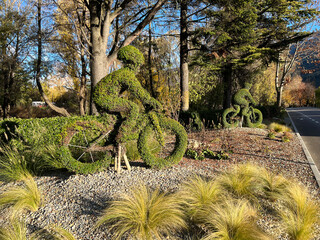 Two wire rods overgrown with green plants cut to look like two cyclists on their bikes in a green landscape on a road