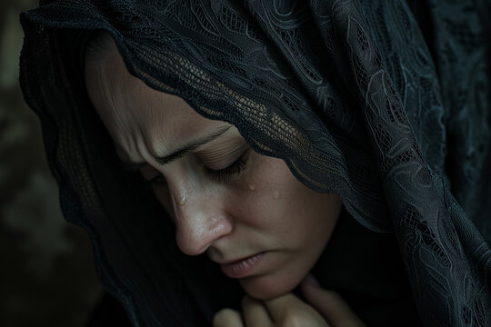Mourning woman praying and crying, young widow bowed in prayer to God, with a black veil as a sign of mourning