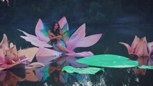 Art Fantasy Woman Little Fabulous Fairy With Butterfly Wings Sits In Water Lily Flower Throne Floating On River Summer Dark Nature Huge Pink Flowers Creative Decor On Lake Blue Fog. Nymph Girl Elf 4k