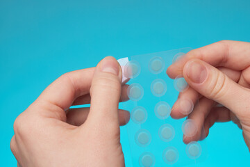 close-up round acne patch on finger on blue background. acne patches for treatment of pimple and ros