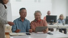 Medium Shot Of Couple Of Retired People Being Surprised And Laughing About Something Funny Looking At Digital Tablet During Group Class