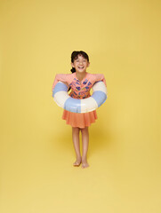 Wall Mural - Little funny happy asian girl in swimsuit jumping up in air with inflatable ring around waist, isolated on yellow studio background. Summertime, vacation an school holidays concept