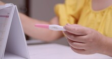 Blurry Close-up Shot Of A Woman Holding The Result Of A Pregnancy Test Kit While Checking The Possible Due Date Of Her Delivery.