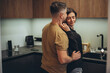 A young couple is standing in the kitchen. The guy sneaks up behind the girl and touches her waist with his hand. The girl, closing her eyes in a half-turn, touches the guy’s cheek with her fingers