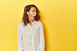 Middle-aged woman on a yellow backdrop being shocked because of something she has seen.