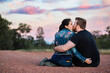 © Austockphoto - Couple in their late twenties sitting together at dusk kissing