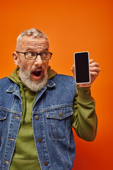 Wall Mural - surprised handsome mature male model in stylish vivid attire looking at smartphone in his hands