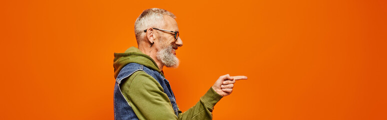 Wall Mural - handsome joyful mature man in vibrant attire posing in profile and pointing in front of him, banner