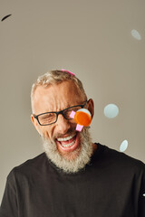 Wall Mural - joyful mature male model in black t shirt with glasses posing under confetti rain with closed eyes