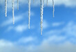 Long crystal icicles hanging down close-up before blurred blue sky with white fluffy clouds 