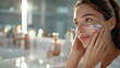 Woman Applying Facial Cream, young woman with a serene expression applies facial cream, illustrating a moment of self-care and beauty routine in a well-lit bathroom