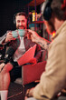 cheerful bearded man with coffee cup in his hand looking at paperwork next to his podcaster