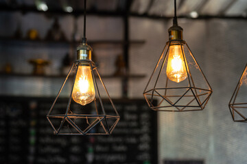 Classic style lightbulb ceiling lamp with iron cage glowing in orange light shade. Interior decoration object photo, selective focus.