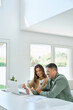 © insta_photos - Happy mature couple calculating money expenses savings using laptop at home. Middle aged man and woman checking receipts for tax refund, paying bills online sitting at table in living room. Vertical.