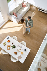 Wall Mural - Happy affectionate romantic middle aged mature couple dancing at home. Senior older man and woman in love standing in modern house living room enjoying dance. Candid photo. Top view, vertical.
