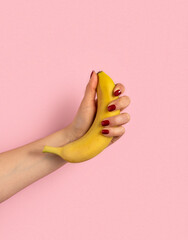 Woman's hand holds banana on pink background.