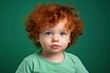 Cute handsome little boy todler with curly red hair and freckles wearing an green T-shirt on an plain green background. Place for text. Studio portrait of happy red-haired child