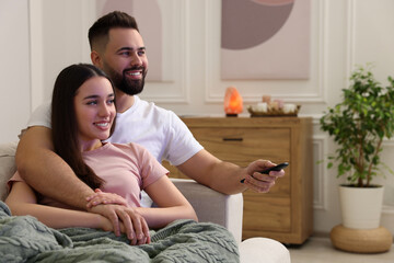 Sticker - Happy young couple watching tv on sofa in living room. Space for text