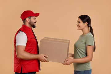 Wall Mural - Smiling courier giving parcel to receiver on light brown background