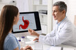 © New Africa - Gastroenterologist showing screen with illustration of human stomach model to patient at table in clinic