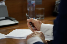 An Elderly Man In A Business Suit With Cuffs, Sitting At A Desk With Pen And Documents. Concept Of Writing A Will, Drafting A Contract Or Filling Out Forms. Photo. No Face. Selective Focus