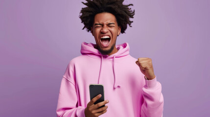 Sticker - excited young man with curly hair in a pink hoodie, holding a smartphone with one hand and making a fist with the other