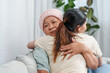 © Ekkasit A Siam - Embracing in warm hug, young woman supports her cancer-stricken mother, conveying love and comfort. Tender moment as daughter hugs her ill mother, both finding solace in embrace, serene indoor setting