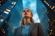 © tong2530 - A confident and professional young businesswoman looking up while standing against contemporary corporate skyscrapers with illuminated facade in financial district in the evening. Low angle side