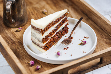 Wall Mural - A piece of carrot cake served on rustic plate placed on bright sunny scene. Layered cake with cream cheese frosting and fluffy biscuit. Served with tea. 